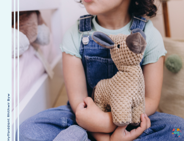 Child wearing blue dungarees holding on to a teddy