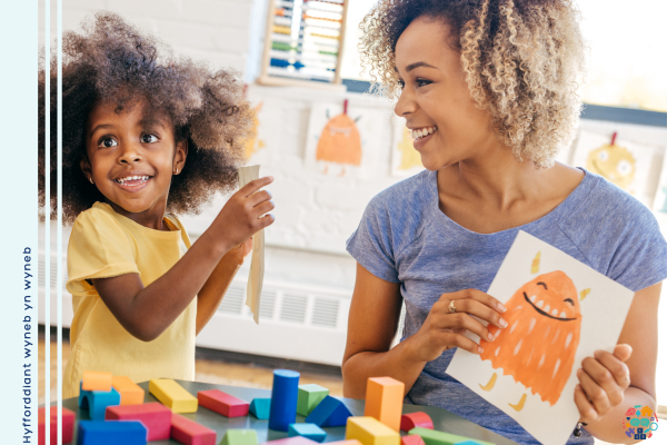 Child shows off her painting to and adult who is also holding up her painting of a yellow monster.