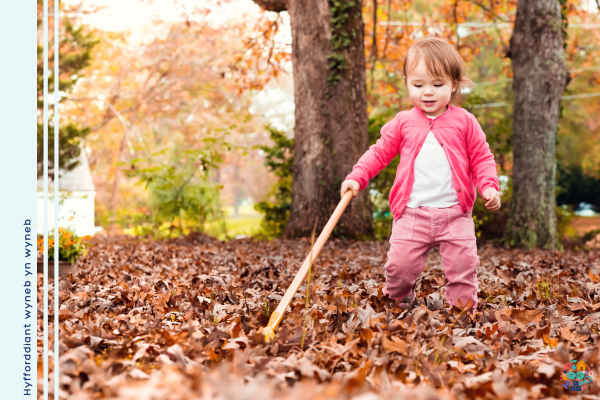 Toddler dressed all in pink holds a stick while walking through leaves