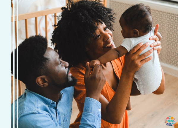 Two adults smile while holding up a baby in the air