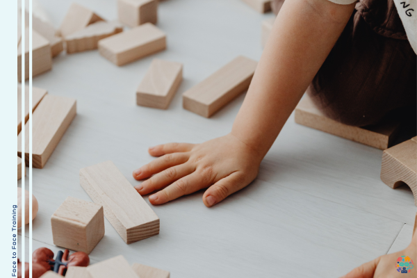 A child's hand leans on the floor with wooden blocks scattered all around