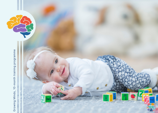 Baby lying on their side holding wooden blocks. They are wearing a big white bow in their hair