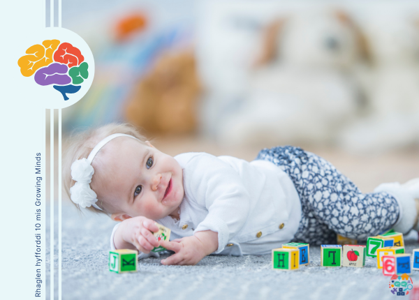 Baby lying on their side holding wooden blocks. They are wearing a big white bow in their hair