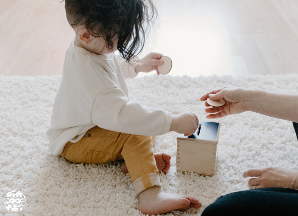 Child putting a wooden coin into a wooden money box