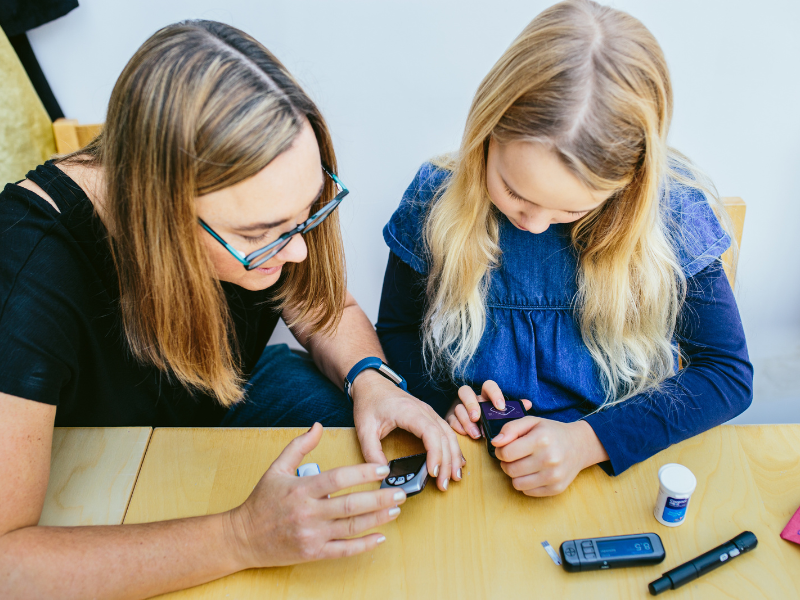 picture shows young girl being shown how to check her insulin levels