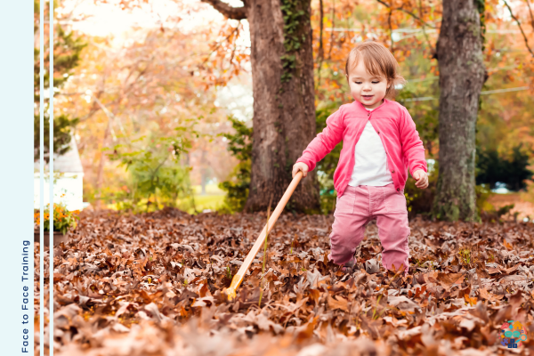 Toddler dressed all in pink holds a stick while walking through leaves