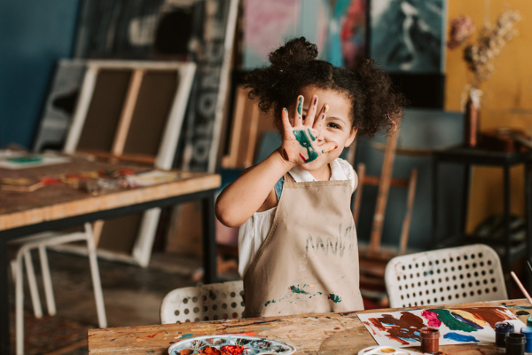 Girl wearing apron holds up hand covered in paint