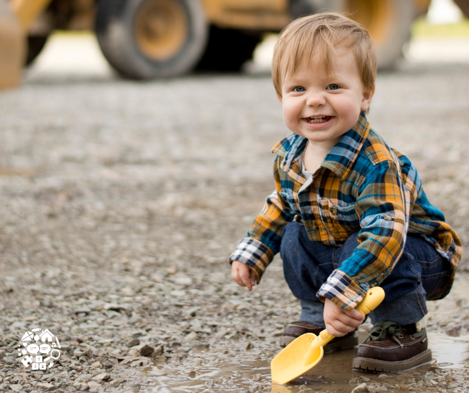 picture is of a toddler digging the ground with a digger in the background