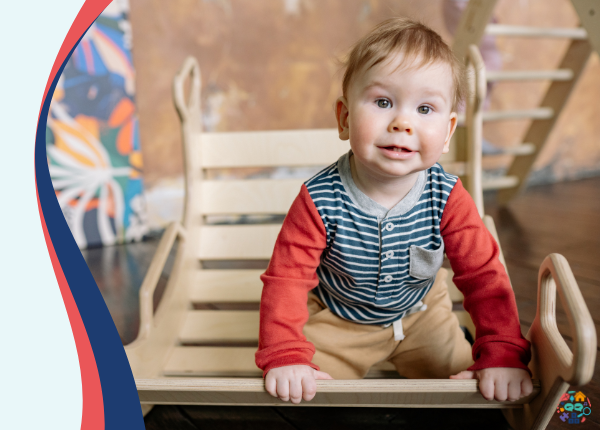 A baby balancing on a rocker. The baby is wearing a blue and red top and is smiling at the camera