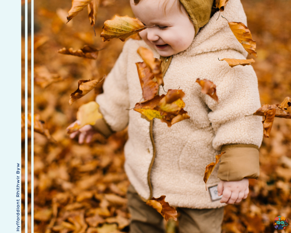 Toddler wearing a white fluffy coat playing in leaves
