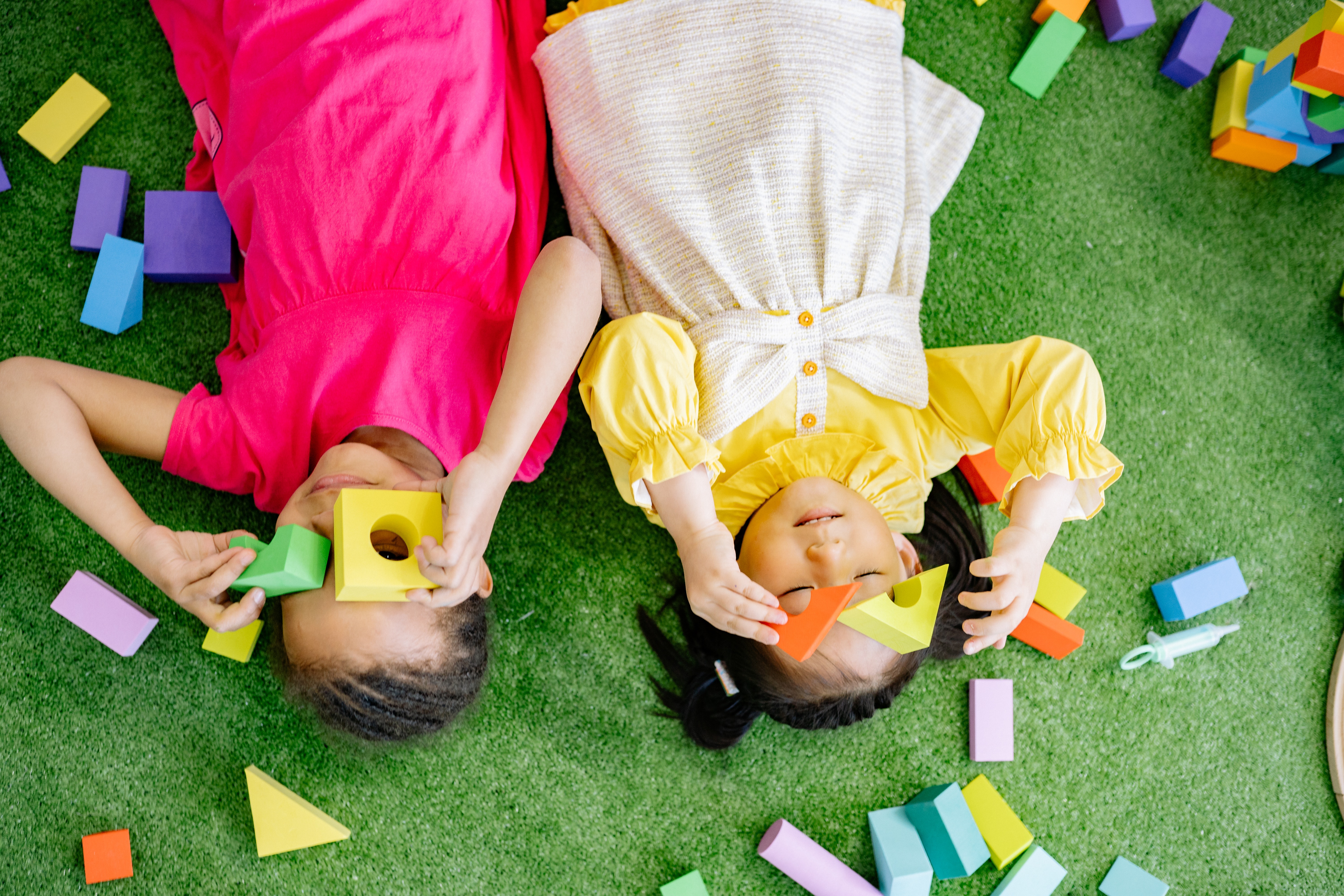 Girls Lying Down On Green Carpet Playing With Wooden Blocks