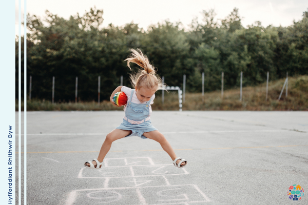Child wearing dungarees is mid jump holding a multcoloured ball