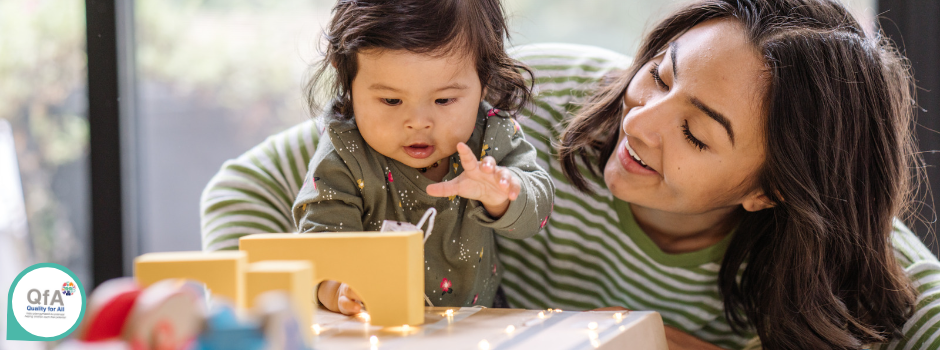 Adult smiling while child reaches for block