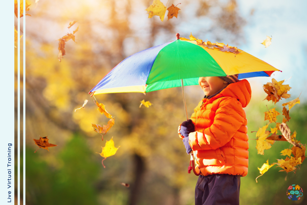 A child wearing a bright orange coat is playing in leaves being shielded by a multi-colour umbrella