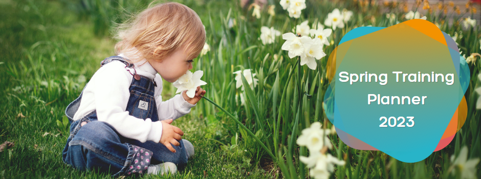 Spring Training Planner 2023 Girl wearing blue jean dungaries is sitting in a field taking the time to smell the white daffodil