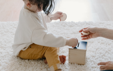 Child putting a wooden coin into a wooden money box