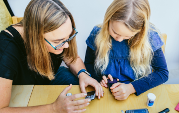 picture shows young girl being shown how to check her insulin levels