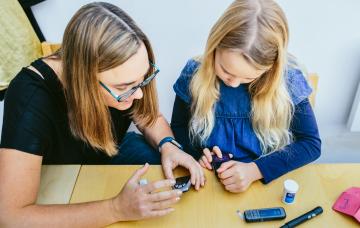 picture shows young girl being shown how to check her insulin levels