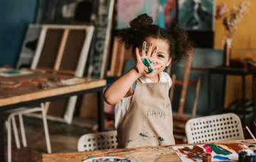 Girl wearing apron holds up hand covered in paint