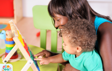 Adult wearing a blue tank top holding child wearing a blue top adds up using an abacus
