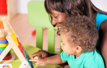 Adult wearing a blue tank top holding child wearing a blue top adds up using an abacus