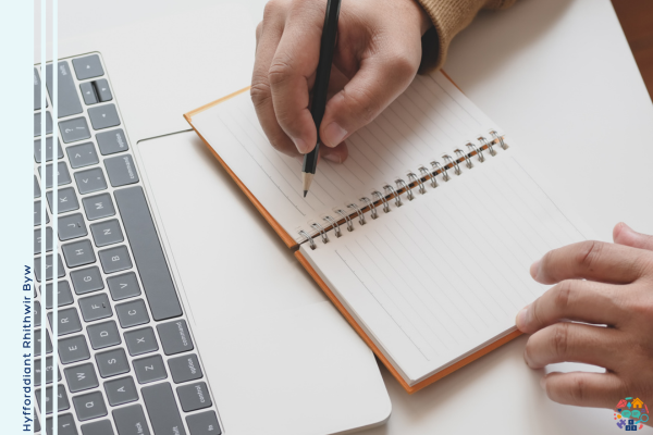 Person taking notes on a notebook resting on a laptop