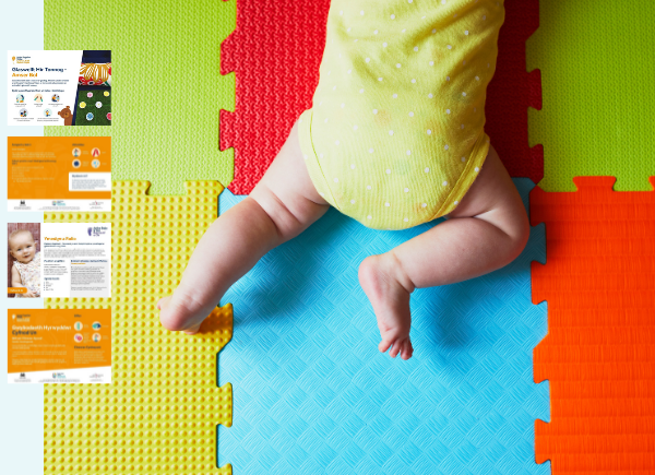 Baby in a yellow and white polka dot babygrow doing tummy time on colourful mats