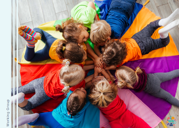 Children laying on a colourful mat in a circle stacking hands